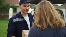 Woman meets a handsome friendly delivery man who gives her a parcel box beside her home. Concept of courier, home delivery, online shopping.