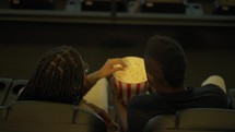 African American young couple came to the movie theatre watching film, eating popcorn from bucket, top view.