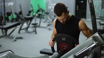 Man Puts Additional Weights on a Barbell. Muscular Fit Guy Performs Leg Exercises.