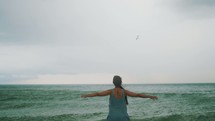 girl standing on a beach with outstretched arms 