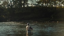 Young fly fisherman casting on a foggy river at sunrise