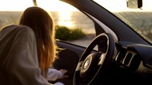 Blonde woman getting into car on the coast during golden hour.