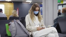 Woman tourist wearing medical protection mask using mobile phone in airport.