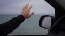 A man's hand is catching the rain out while driving a car on a rainy day.