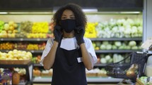 Portrait of happy African American female worker in black mask and gloves standing in supermarket, taking off protection mask.