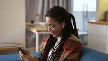 Young woman using smartphone at home on a couch, side view.