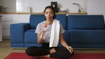 African american woman drinking water after workout at home on yoga mat.