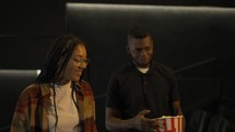 African American young couple came to the movie theatre watching film, eating popcorn from bucket.