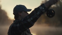 Young fly fisherman casting on a foggy river at sunrise