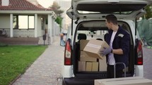 Young handsome Caucasian delivery man putting boxes in van delivering shipment. Male post office worker Courier concept.