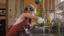 a toddler girl washing dishes 