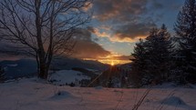 idyllic sunset in a snowy landscape with moving colorful clouds, trees and a snowman
