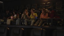 Group of young friends in a movie theater, came watching a movie on a big screen, talking to each other.