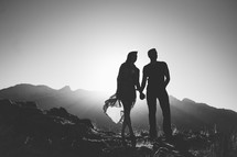 Silhouette of a couple holding hands while standing on a mountain.