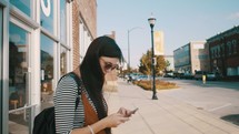 woman texting standing on a downtown sidewalk 