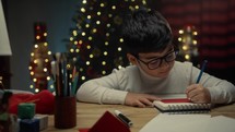 Young boy writing Christmas letter at his desk
