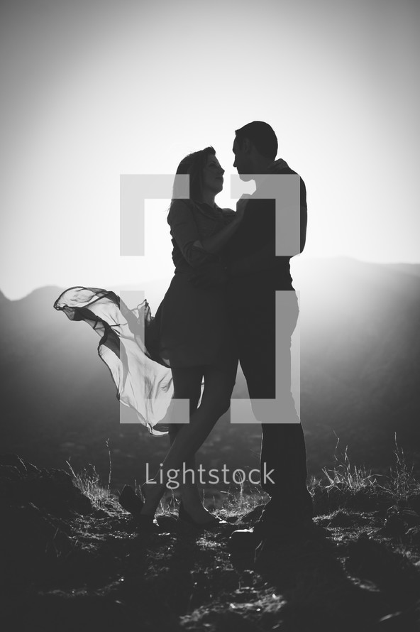Silhouette of man and woman, dress blowing in the wind, mountains in the distance