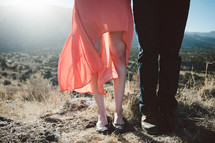 legs of a man and woman, standing on a rocky, weedy mountain top