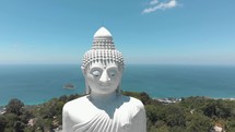Majestic Big Buddha sitting atop Nakkerd Hill looking after Chalong in Phuket, Thailand - Aerial Orbit Wide panorama reveal
