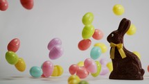 falling Easter eggs around a chocolate bunny on a white background