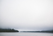 A lake surrounded by a foggy, tree covered shoreline.