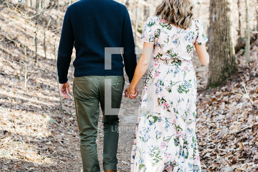 a couple holding hands walking in the woods 