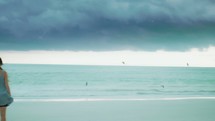 woman standing on a beach under storm clouds 