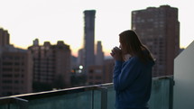 Woman drinking a hot beverage on a balcony in the city