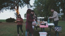 people getting food around a picnic table outdoors 