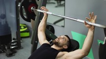 Men laying and working out barbell bench press in the gym.