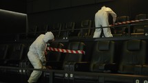 Quarantine due to coronavirus pandemia - two men in protection costume stretching warning ribbons on seats.