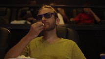 A man in 3d glasses watching movie at the cinema and eating popcorn.