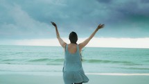 girl standing on a beach with raised hands 