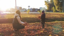 Mother and little boy throws a pile of leaves overhead and watches them fall. Kid playing with the golden leaves in autumn park. Happy family on autumn walk. People in park. Happy family concept.