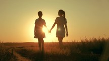 Friendly family. Silhouettes mother and daughter holding hands at sunset in the meadow. Happy mom and daughter walk holding hands towards the sunset in summer. Freedom happiness concept.