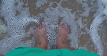 Ocean waves washing over a man's feet in the sand