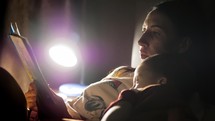 Child reading book in bed. Mother reading a bedtime story to her little son in bedroom. Education for children. Family before going to bed mother reads to her son book near a lamp in the evening.