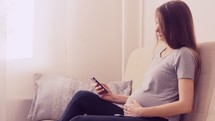 Pregnant woman rubbing her belly and scrolling on her phone.