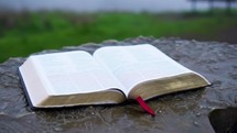 orbiting shot of an open bible on an outdoor podium on a foggy day.