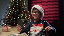 Little Kid typing on smartphone Under Christmas tree 