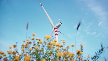 Wind power plant turbine for electric clean energy near a park of flowers at sunset
