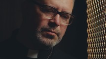 Empathic Catholic priest sitting in confessional booth, listening to penitent with understanding and talking through latticed screen. Close-up view
