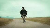 Man with poncho walks on dirt road