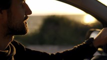 Bearded man focusing driving a car along the coast, golden hour, blurred backgraund.