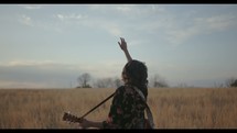a woman standing in a field holding a guitar with her arm raised 