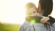 Happy harmonious family in the open air. The mother holds the child in her arms, hugging him. A little boy experiences emotions of love and happiness. Mother hugging and kissing her son on the nature.