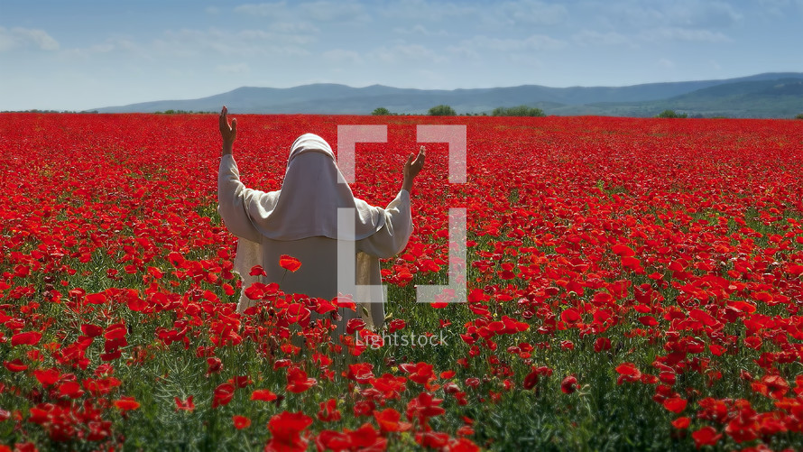 A nun in white praying in the field of vibrant red poppy flowers.
