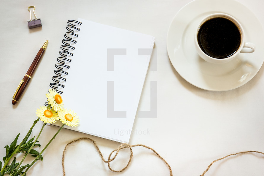 blank pages in a notebook, pen, clip, coffee cup, twine, spring flower on a white background 