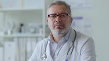 Portrait of Mid-Aged Male Physician Sitting at Workplace in Clinic
