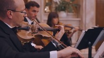 A stringed quartet plays music - focused on the violinist.

